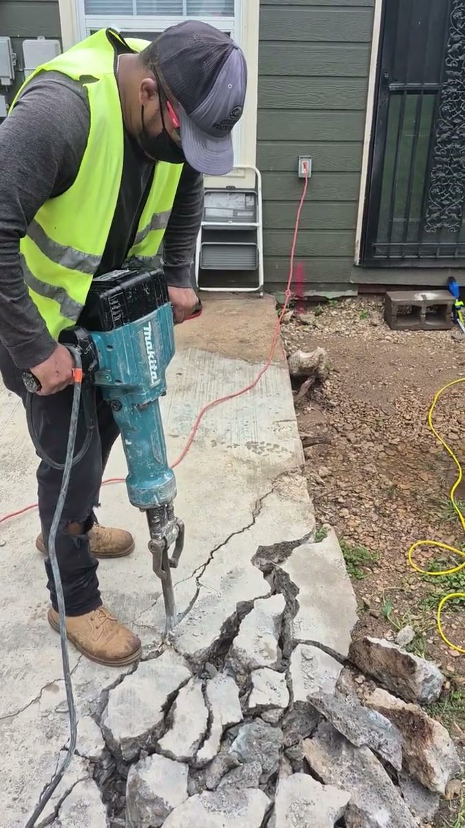 Crew member breaking up a concrete walkway with a jackhammer