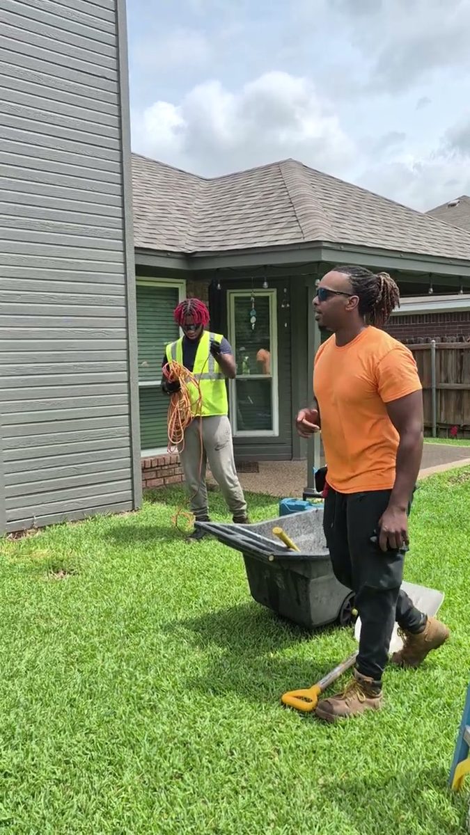 Munachi and a crew member working a backyard job with a wheelbarrow and ladder