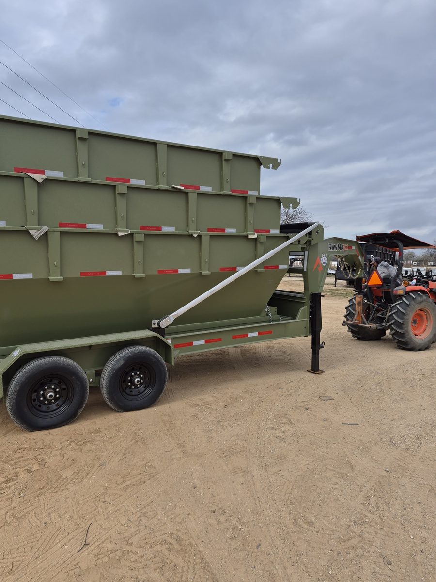 Green roll-off dumpster staged beside a tractor on a job site