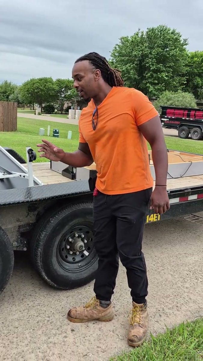 Munachi standing beside his equipment trailer in a customer's driveway